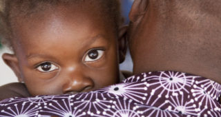 Close-up shot of a Black baby’s face held by an adult